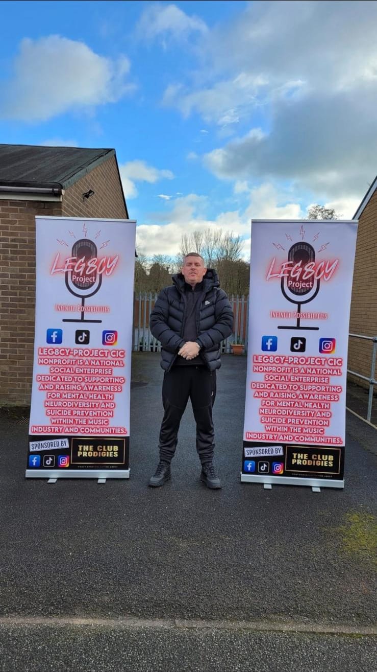 Scott Glover, founder, standing between two Leg8cy Project CIC banners